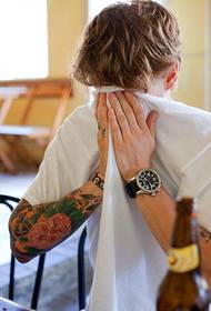 Europietiškas gražus vaikinas Stilinga kaukolės ir gėlių tatuiruotė