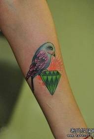 Ramię dziewczyny z kolorowym wzorem tatuażu z ptakiem i diamentem