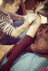 Knappe tattoo kunstenaar dij bloem tattoo scène foto