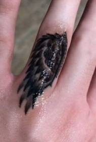 Minimalistinis piršto tatuiruotės pirštas ant juodų sparnų tatuiruotės paveikslėlio