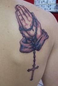 На раменима смеђе руке за молитву с крижном тетоважом