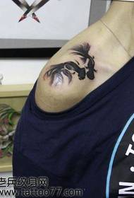 Malowanie tuszem na ramieniu mały wzór tatuażu złotej rybki