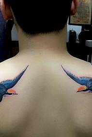 Two small swallows tattooed in the back wearing a floral dress