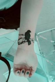 ручна црна врана која сједи на узорку тетоваже на грани