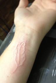 modello del tatuaggio della piuma di contorno bianco del polso della ragazza