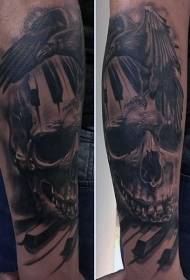 braccio corvo grigio nero con motivo tatuaggio teschio e pianoforte chiave