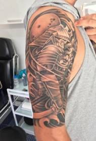 Tattoo Samurai, донишҷӯи мард, бозуи калон оид ба гулҳои гелосӣ ва тасвири ашёи самурайӣ