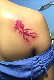 tattoo ndogo ya dhahabu ya samaki huanguka chini ya bega la msichana