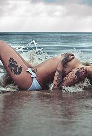Sexet tatoveringsskønhedsmønsterbillede liggende på havstranden