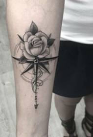 Braccio della ragazza sulla bussola pungente nera e sull'immagine letteraria del tatuaggio del fiore della pianta