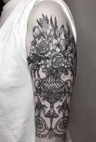 Krahu i Vajzës në vazo të zeza me prizë të bimëve dhe fotografia e tatuazhit me lule